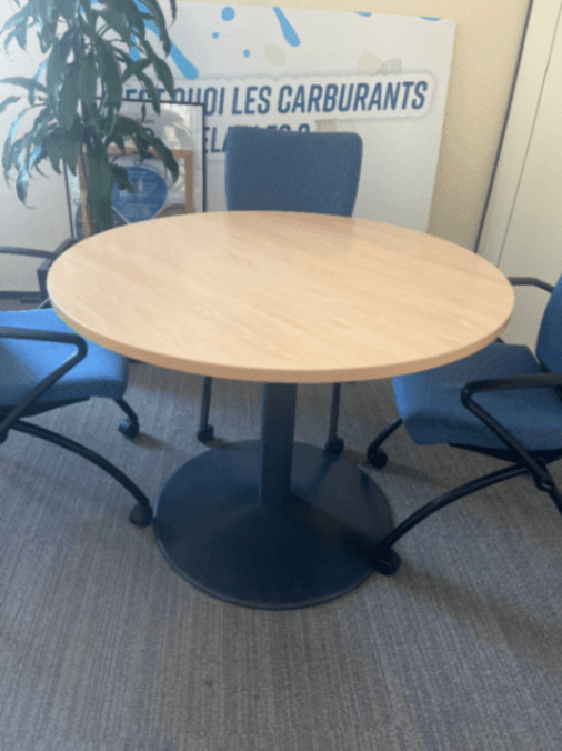 Table ronde en bois stratifié avec pied noir et petit dommage sur le plateau