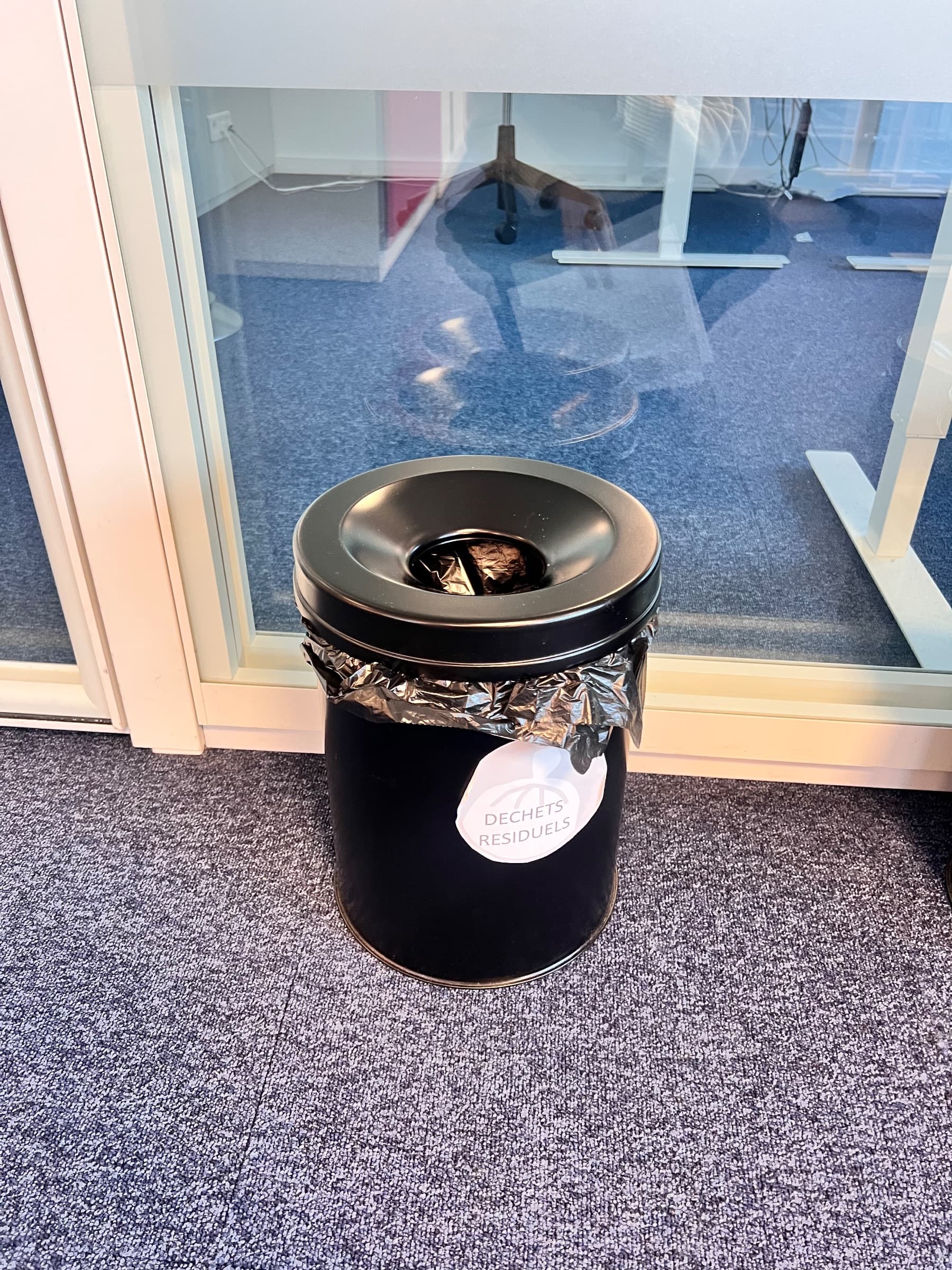 Black metal trash can with a lid and waste label