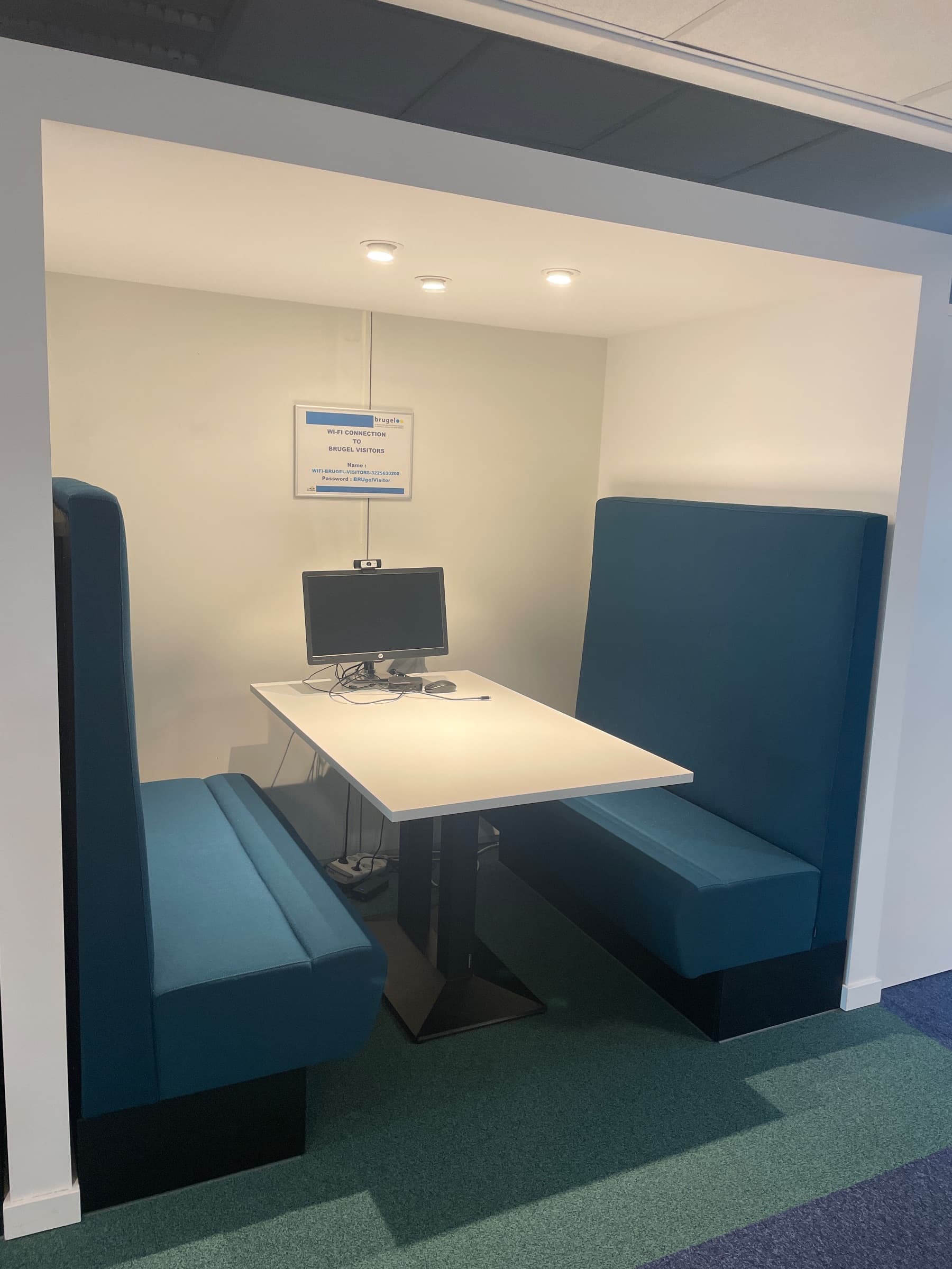 Teal stoffen vergadercabine met witte tafel en geïntegreerde technologie